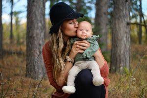 woman in red long sleeve shirt carrying baby in green jacket
